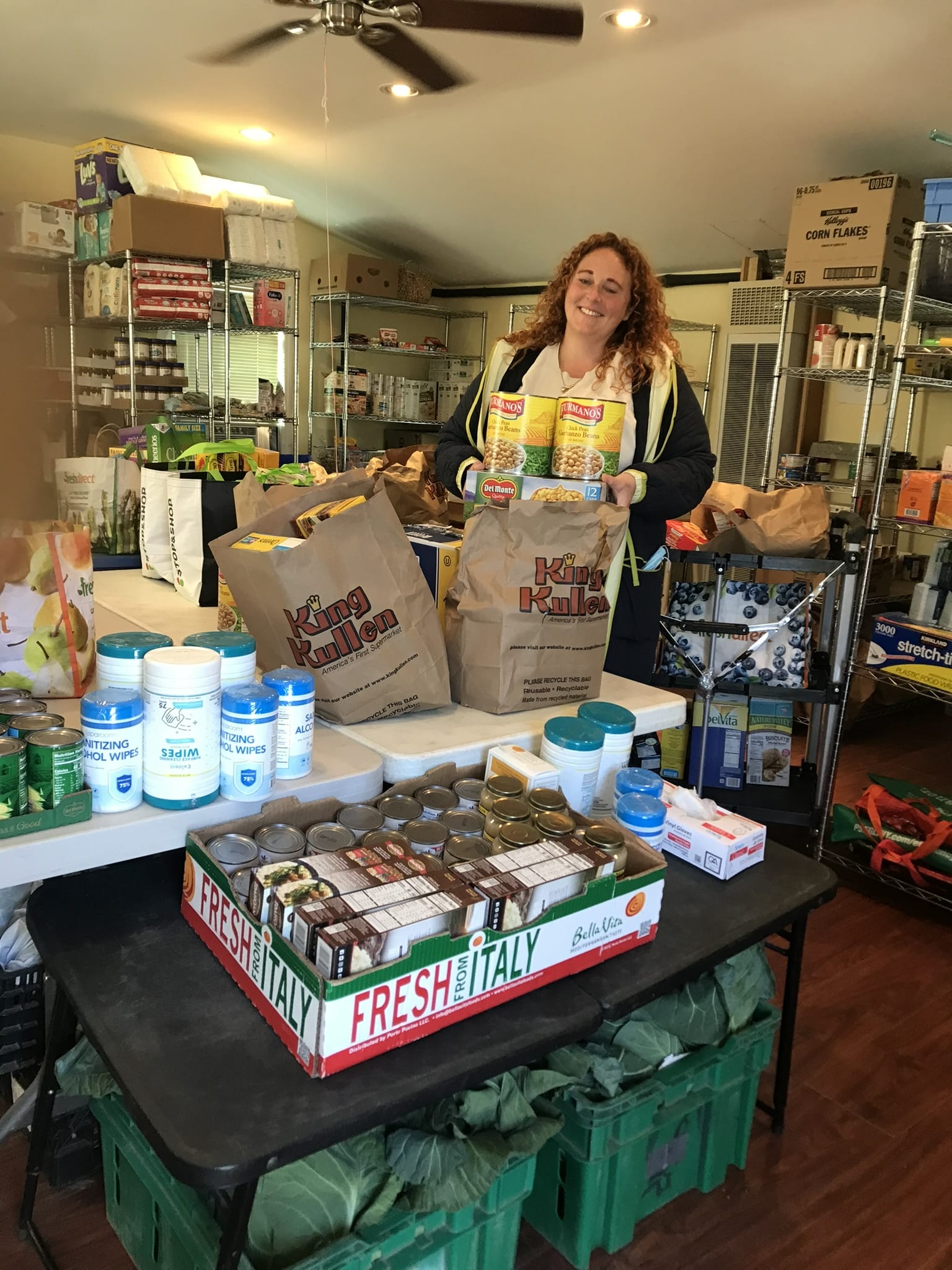 A smiling person behind a table of groceries at the pantry